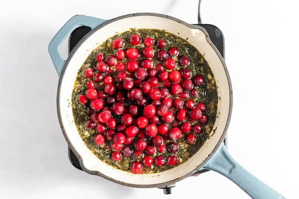 Image, taken from above, shows cranberries in a skillet simmering with sauce ingredients