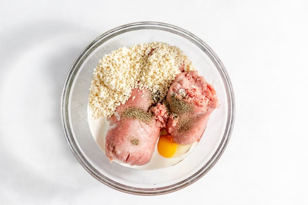 Image, taken from above shows a glass bowl full of ingredients for making meatballs