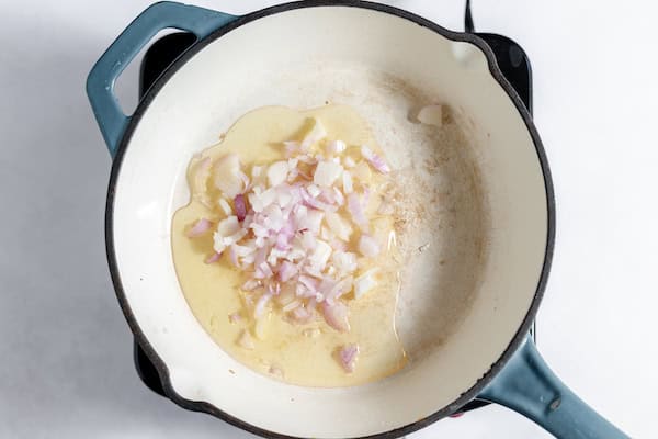 Image, taken from above shows shallots sauteed in a pan with oil