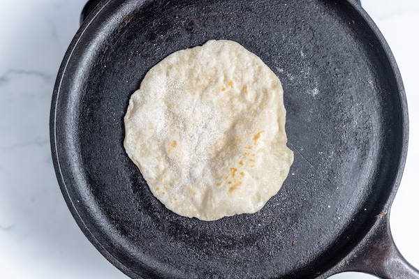 Image, taken from above shows a tortilla cooking on cast iron skillet.