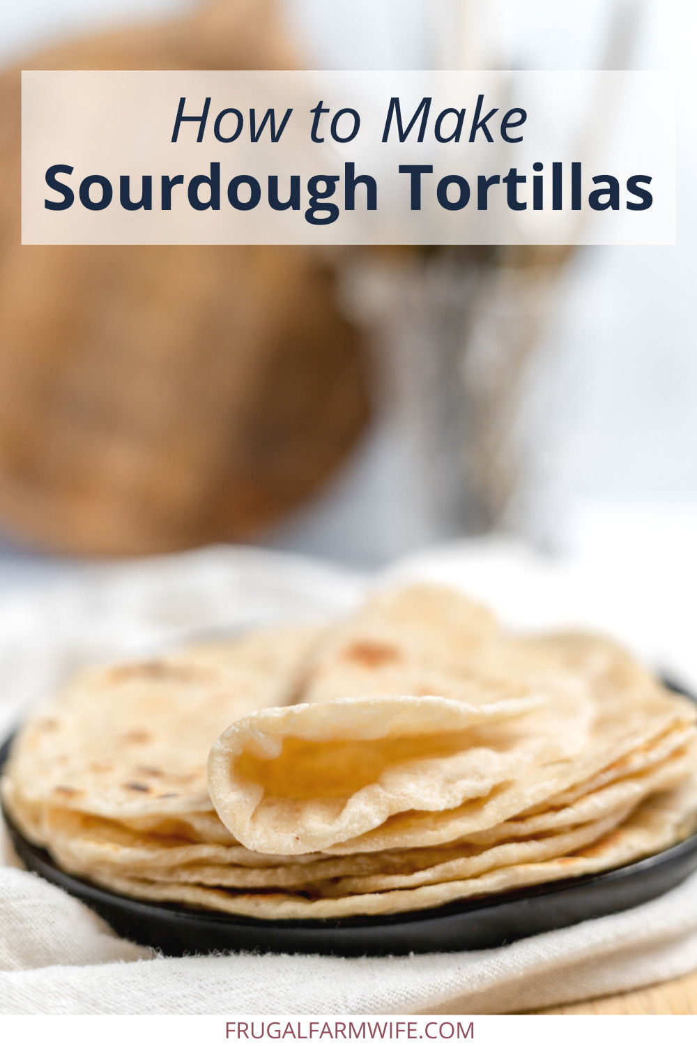 Image shows a black plate on a white towel with sour dough tortillas stacked on it. The top tortilla is folded in half. Text overlay reads "How to Make Sourdough Tortillas"