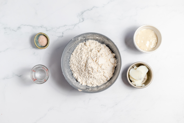 Image, taken from above, shows several bowls with the ingredients to make sourdough tortillas.