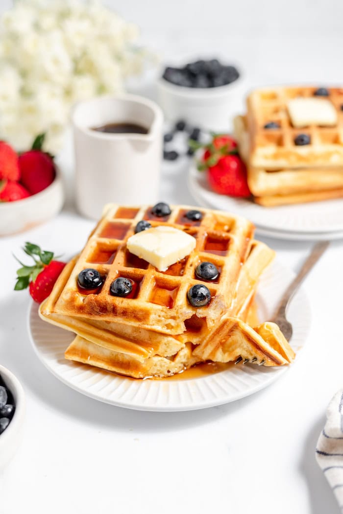 Image shows a fork on a plate taking a bite out of sourdough waffles covered in butter and blueberries.