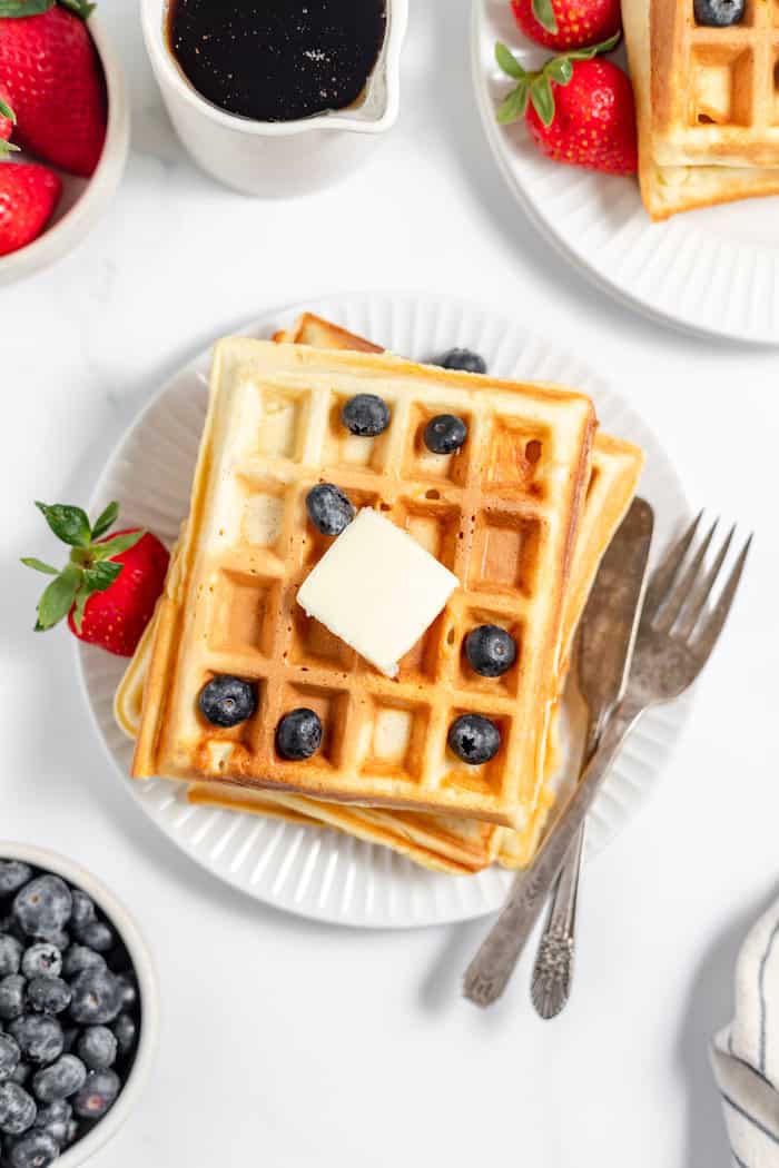 Image, taken from above shows sourdough waffles on a white plate served with syrup and berries