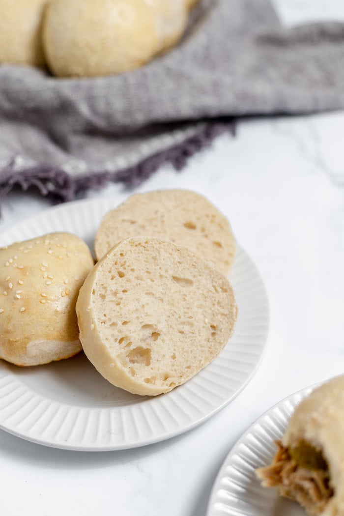 Image shows a dinner table with barbecue sandwiches and sourdough hamburger buns. One bun is sliced in half on a plate.