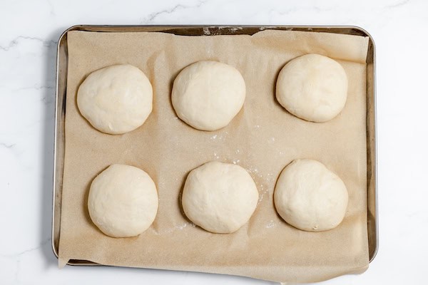 Image, taken from above, shows sourdough buns risen and ready for the oven on a cookie sheet