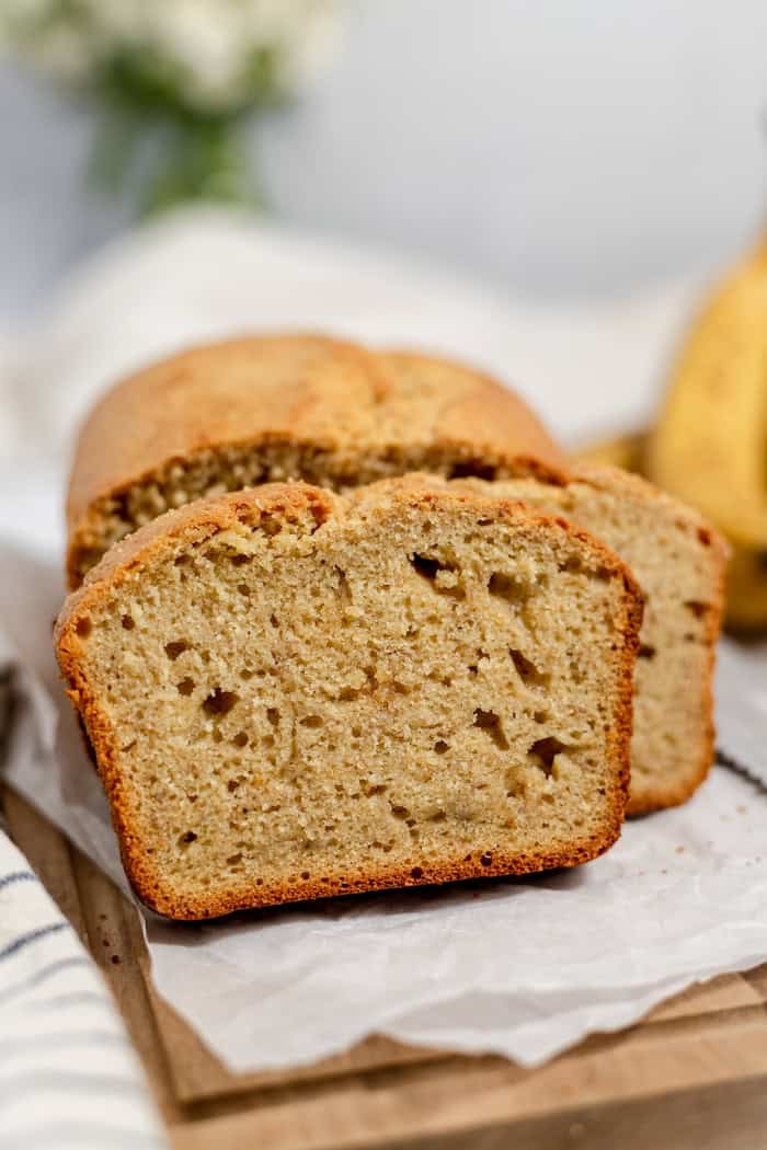 Image shows a loaf of sourdough banana bread, sliced on a wooden cutting board