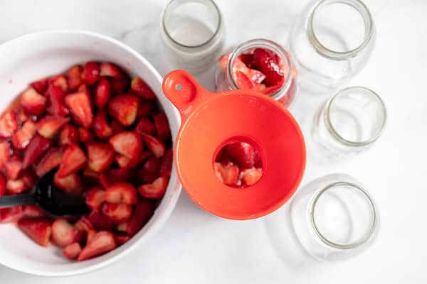 Image, taken from above, shows jars being filled with strawberries using a canning funnel.