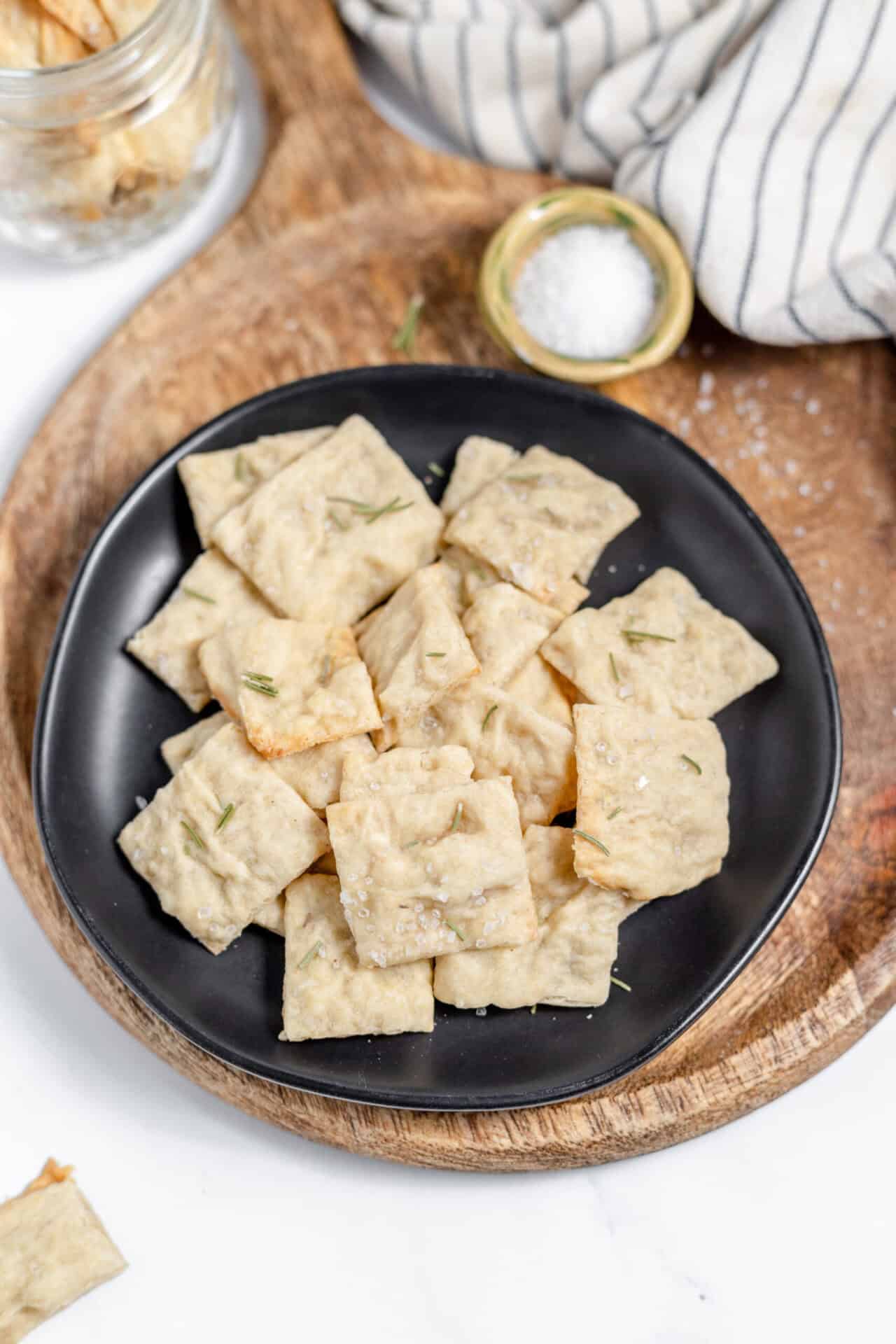Image, taken from above, shows crackers made with sourdough and rosemary on a black plate.