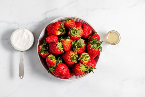 Image, taken from above, shows the ingredients you'll need to can strawberries, in bowls on a counter. 