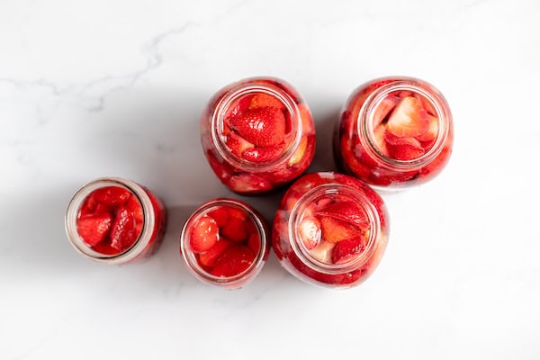 Image, taken from above, shows jars full of strawberries to be canned on a counter. 