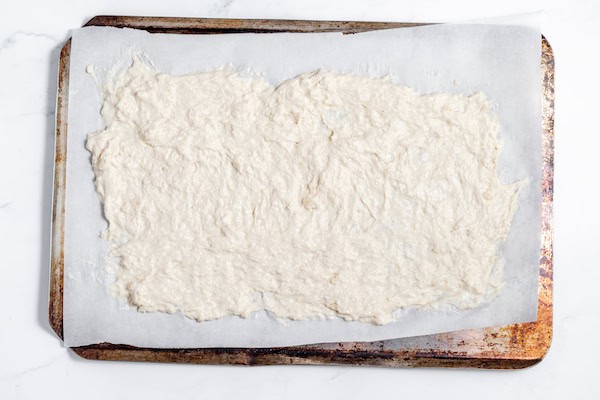Image, taken from above shows cracker dough spread out on a baking sheet