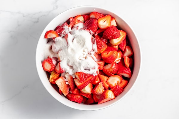 Image, taken from above shows sliced strawberries in a bowl with sugar sprinkled on top.