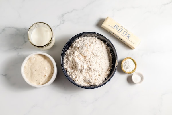 sourdough starter, flour, baking powder, salt, baking powder, butter, and milk on a table