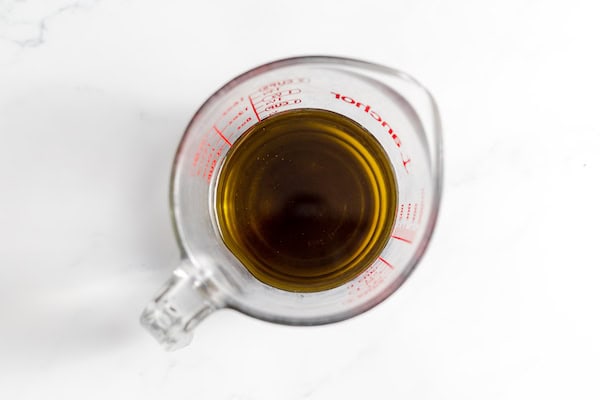Image, taken from above, shows a measuring cup full of herbal infused oil.