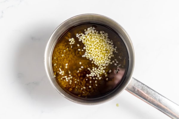 Image, taken from above, shows a pan with herbal oil and beeswax pellets in it.