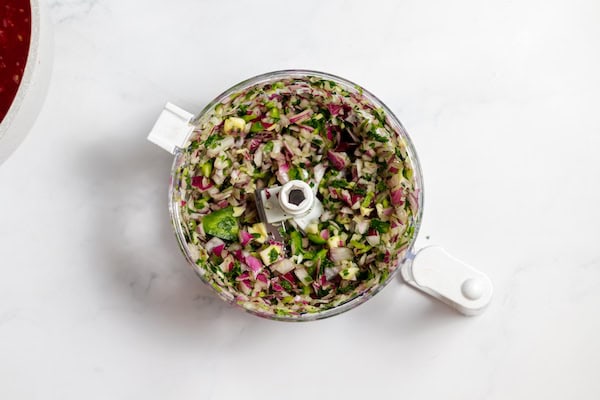 Image, taken from above shows chopped vegetables in food processor on a counter.