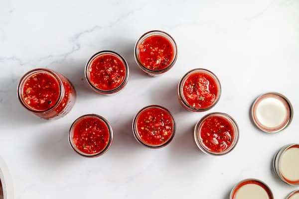 Image, taken from above, shows several canning jars full of salsa on a white counter top. 