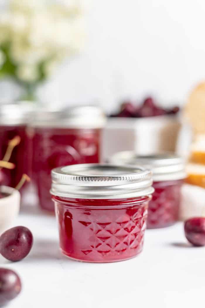jars of jam on a table with cherries