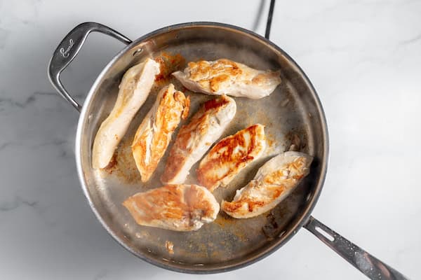 Photo, taken from above, shows several pieces of chicken being seared to a golden brown in a skillet.