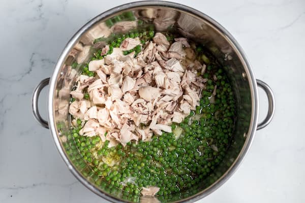 Image, taken from above, shows chicken and peas added to soup in a large pot.