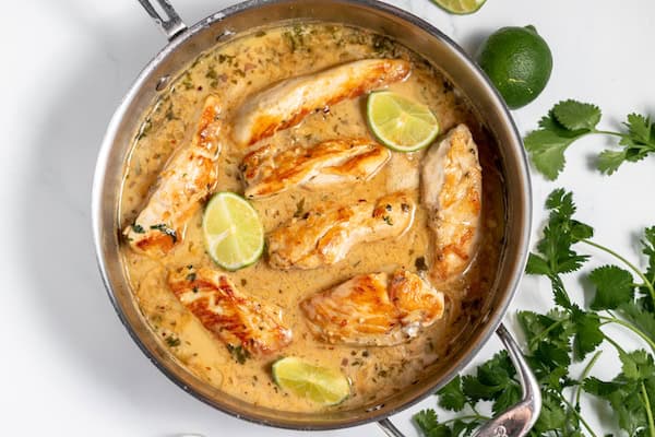 Image, taken from above shows the chicken with coconut and lime in a skillet after the recipe is fully prepared