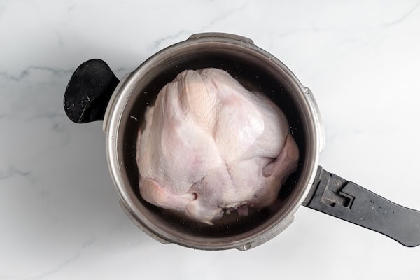 Image, taken from above, shows a chicken being cooked in a pot. 