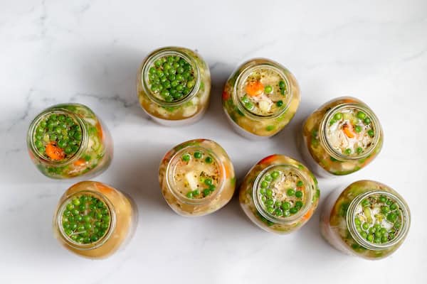 Image, taken from above, shows several jars of chicken soup laid out on a counter. 