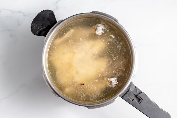 Image, taken from above, shows a chicken in a pot covered in broth.
