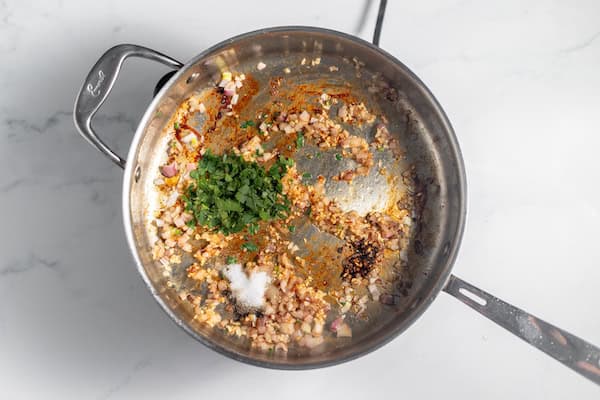 Image, taken from above, shows shallots, garlic, herbs, and seasonings in the same skillet the chicken had been cooked in