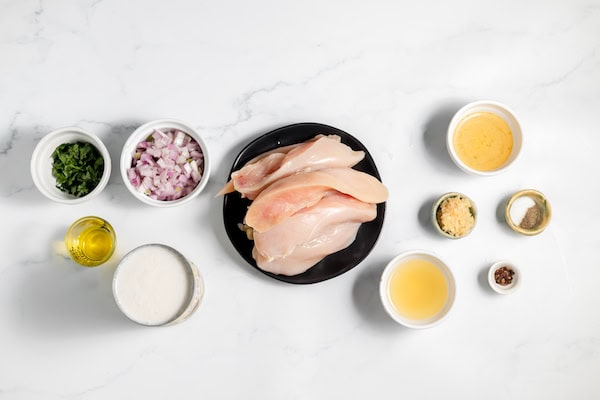 Image, taken from above, shows all the ingredients needed to make Coconut Lime Chicken laid out on a white counter in small dishes and bowls. 