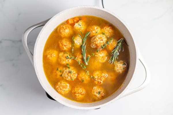 Image, taken from above shows meatballs in broth with rice, vegetables, and herbs in a large pot.