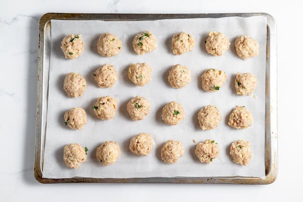 Image, taken from above shows raw meatballs on a baking tray.