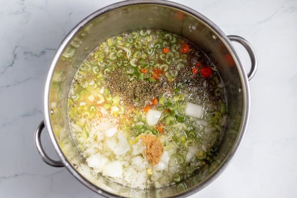 Image, taken from above, shows vegetables and chicken broth in a large pot.
