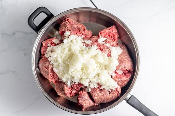 Image, taken from above, shows ground beef and onions cooking in a skillet.