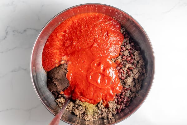 Image, taken from above, shows tomato sauce added to the chili ingredients in a bowl.