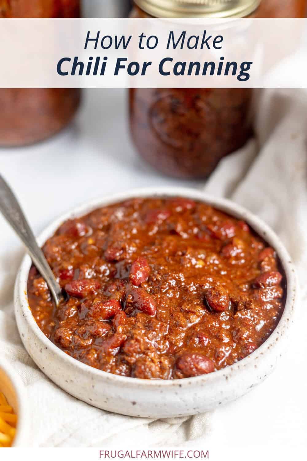 Image shows a bowl of chili with a spoon in it. Several jars of canned chili sit behind it. Text above reads "How to Make Chili for Canning."