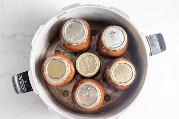 Image, taken from above, shows several jars of chili in a pressure canner.