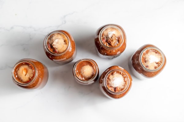 Image, taken from above, shows several jars of chili topped with salt before the jars are sealed. 