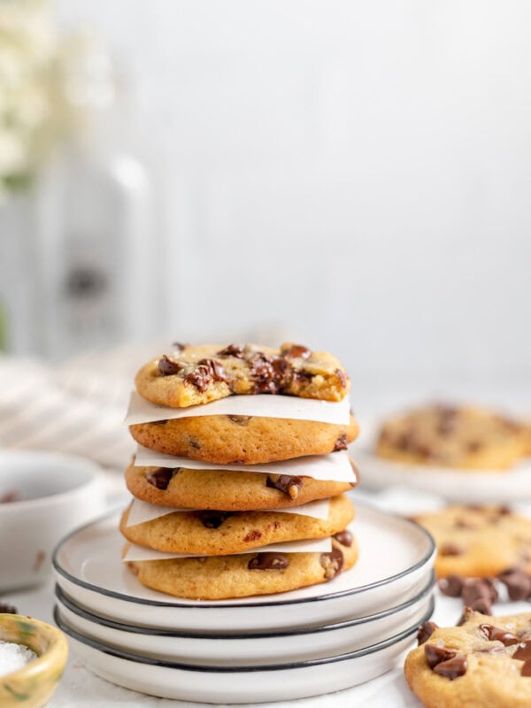 Image shows sourdough cookies stacked on a plate with parchment paper between each cookie. The top cookie has a bite taken out of it. 
