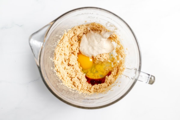 Image, taken from above, shows the sourdough starter added to cookie dough in a glass mixing bowl.