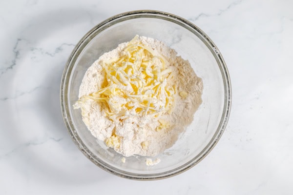 Image, taken from above, shows butter grated into flour mixture in a large glass bowl.