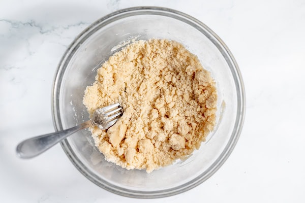 Image, taken from above, shows a shortbread crust mixed in a glass bowl with a fork. 