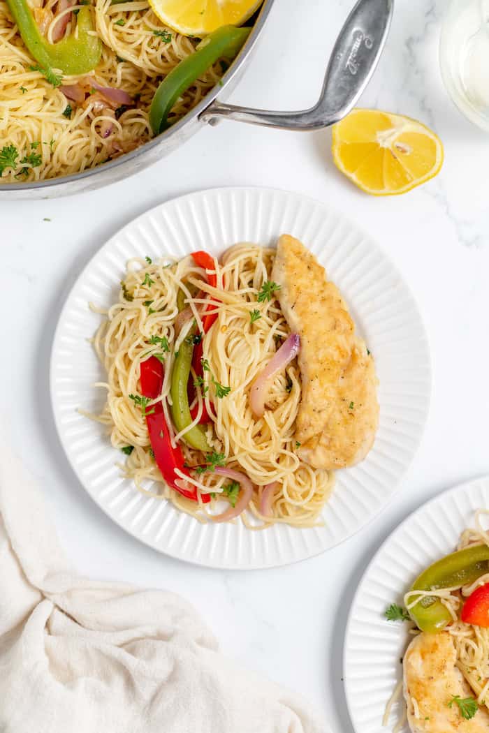 Image, taken from above, shows two plates of chicken scampi with angel hair pasta, and a larger pot of more chicken scampi.