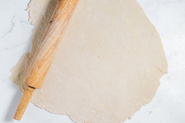 Image, taken from above, shows rolled out pie crust dough with a rolling pin.