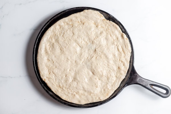 Image, taken from above, shows sourdough rolled out on prepared pizza pan to bake