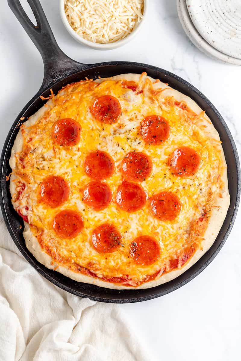 Image, taken from above, shows cooked sourdough pizza on a skillet served with parmesan cheese
