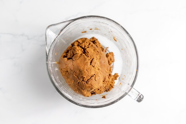 Image, taken from above, shows a glass mixing bowl of gluten free gingerbread dough in a ball shape