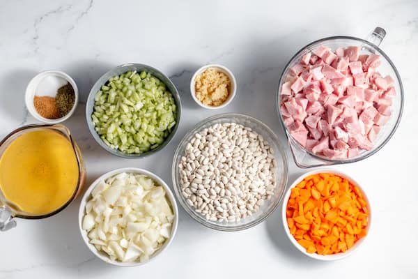 Image, taken from above, shows several bowls of ingredients for making and canning ham and bean soup.
