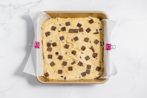 Image, taken from above, shows banana bars batter in pan lined with parchment paper, with chocolate chips on top.
